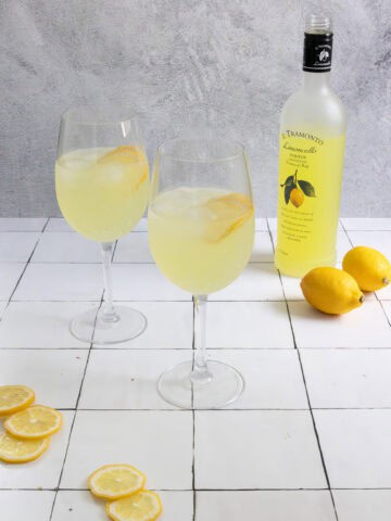 Lemoncello spritz cocktails in wine glasses with bottle of liqueur in background.