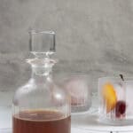 Old fashioned cocktail in pitcher, with two chilled rocks glasses next to it.