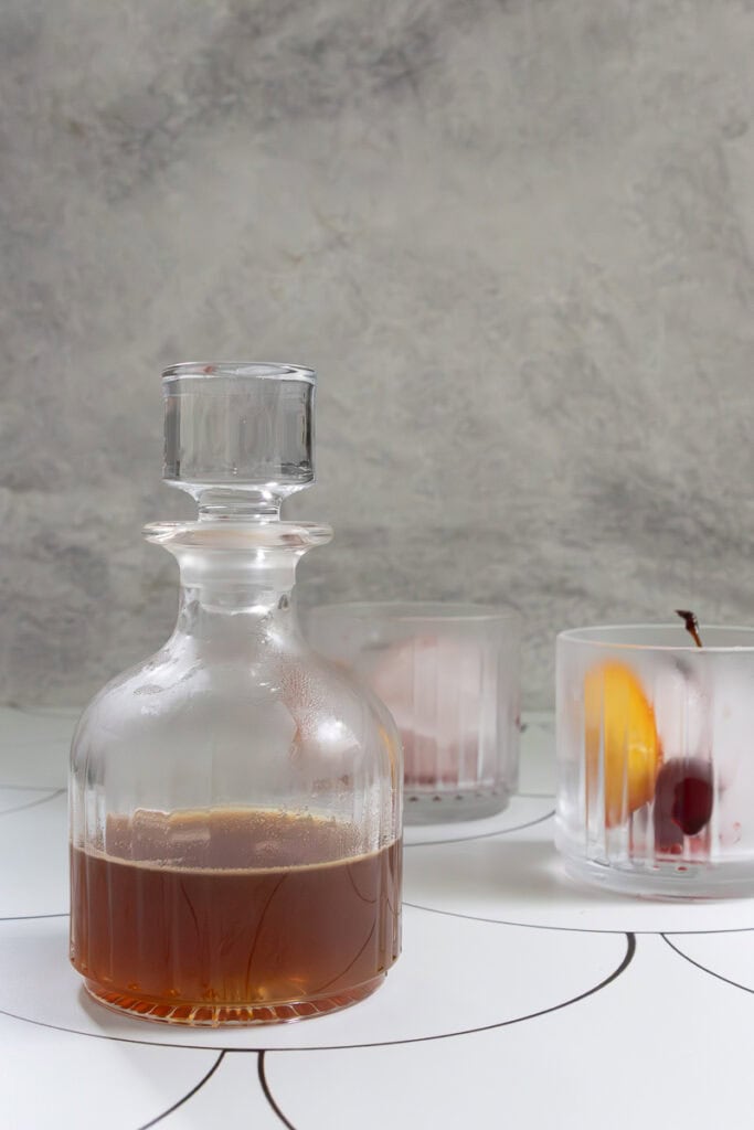 Old fashioned cocktail in pitcher, with two chilled rocks glasses next to it.