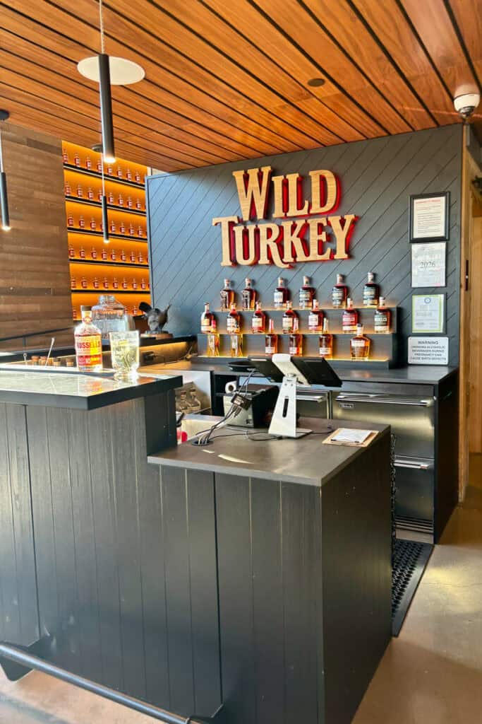Checkout register at Wild Turkey bar with various bourbon bottles on display in background.