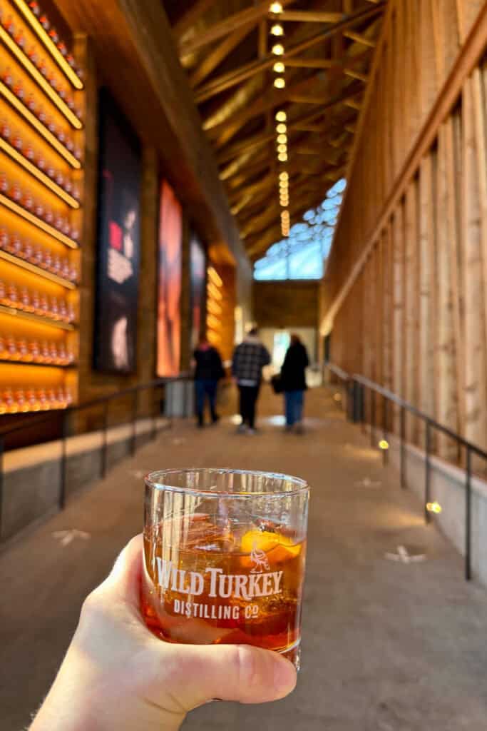 Cocktail in hand with view of distillery visitor center in background.