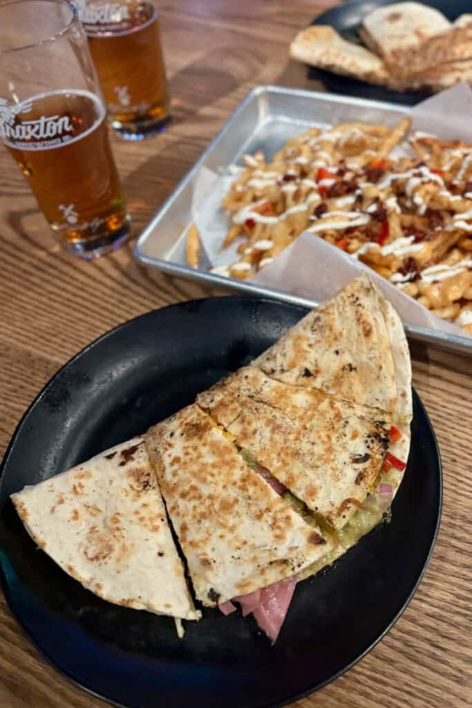 Sliced quesadilla with tray of loaded fries and beer glasses in background.