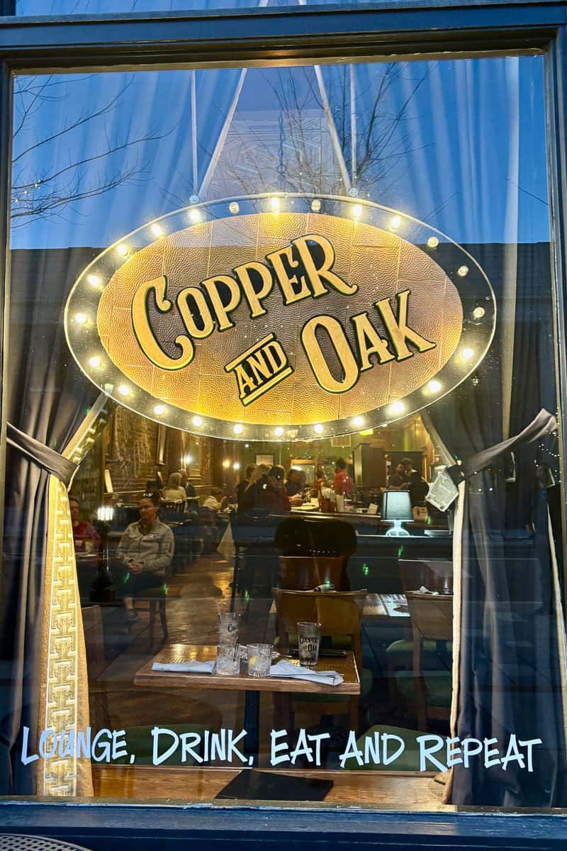 Lighted Copper and Oak sign inside restaurant window.