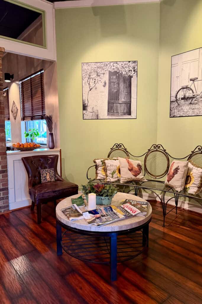 Chair and bench placed in corner of Brasserie Provence with black and white wall art and round table with magazines.