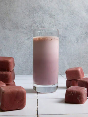 Chocolate cherry smoothie in glass surrounded by smoothie cubes.