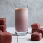 Chocolate cherry smoothie in glass surrounded by smoothie cubes.