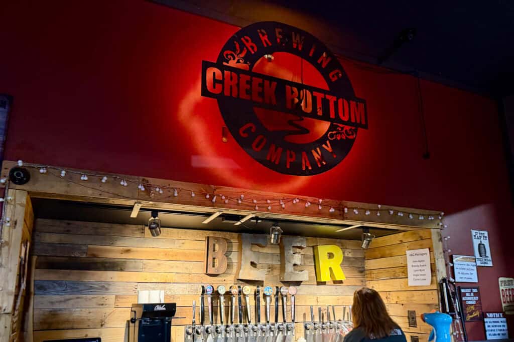 Beers on tap with stenciled Creek Bottom Brewing logo on above wall.