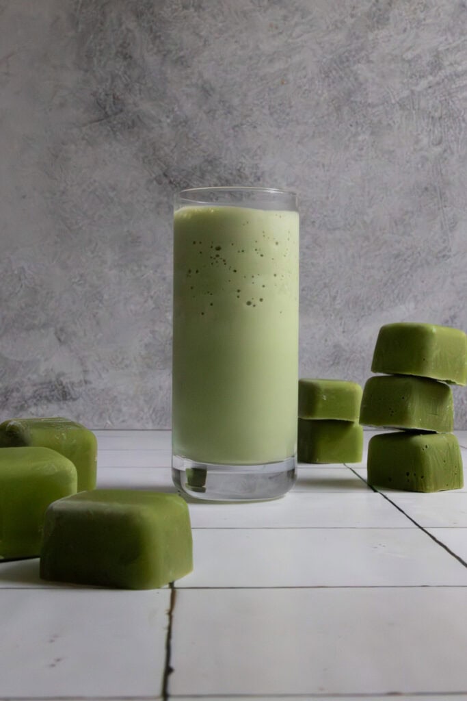 Green smoothie in glass, surrounded by smoothie cubes.