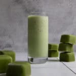 Green smoothie in glass, surrounded by smoothie cubes.