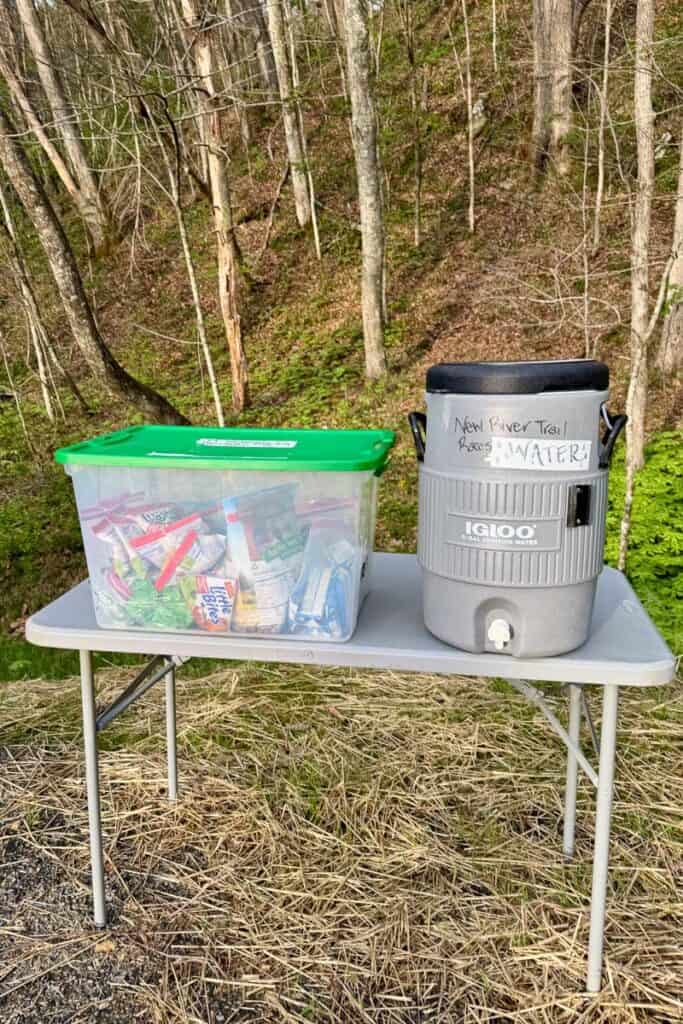 Bin of packaged snacks next to water cooler for runners in New River Trail Races.