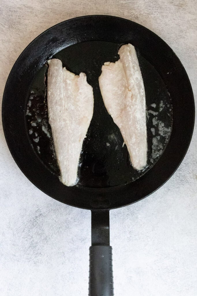 Fish fillets dusted with flour cooking in skillet.