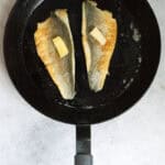Fish fillets in skillet flipped skin-side-up with pats of butter on top.