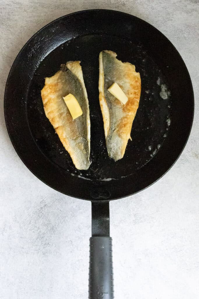 Fish fillets in skillet flipped skin-side-up with pats of butter on top.