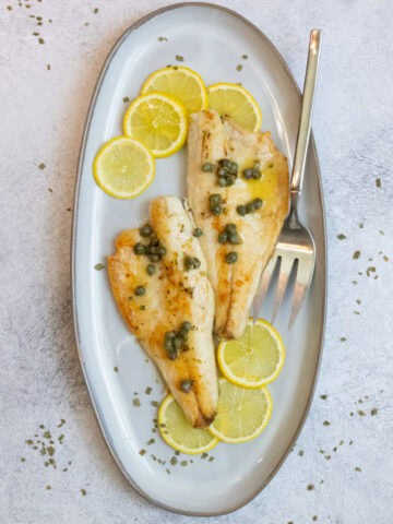 Pan-seared branzino fish fillets on plate with lemon and caper sauce.