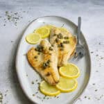 Pan-seared branzino fish fillets on plate with lemon and caper sauce.