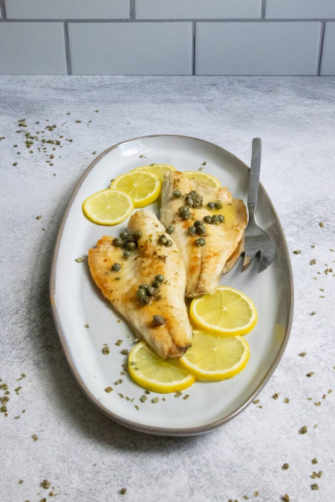 Pan-seared branzino fish fillets on plate with lemon and caper sauce.