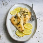 Pan-seared branzino fish fillets on plate with lemon and caper sauce.
