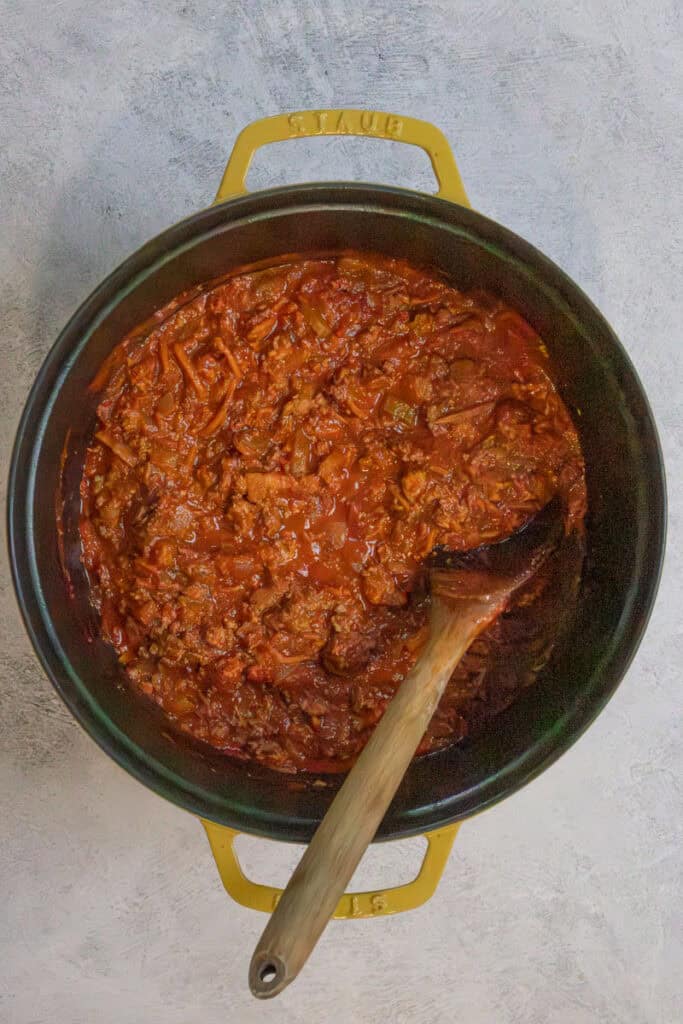 Tomato puree, tomato paste, and broth added to cooked meat in pot.