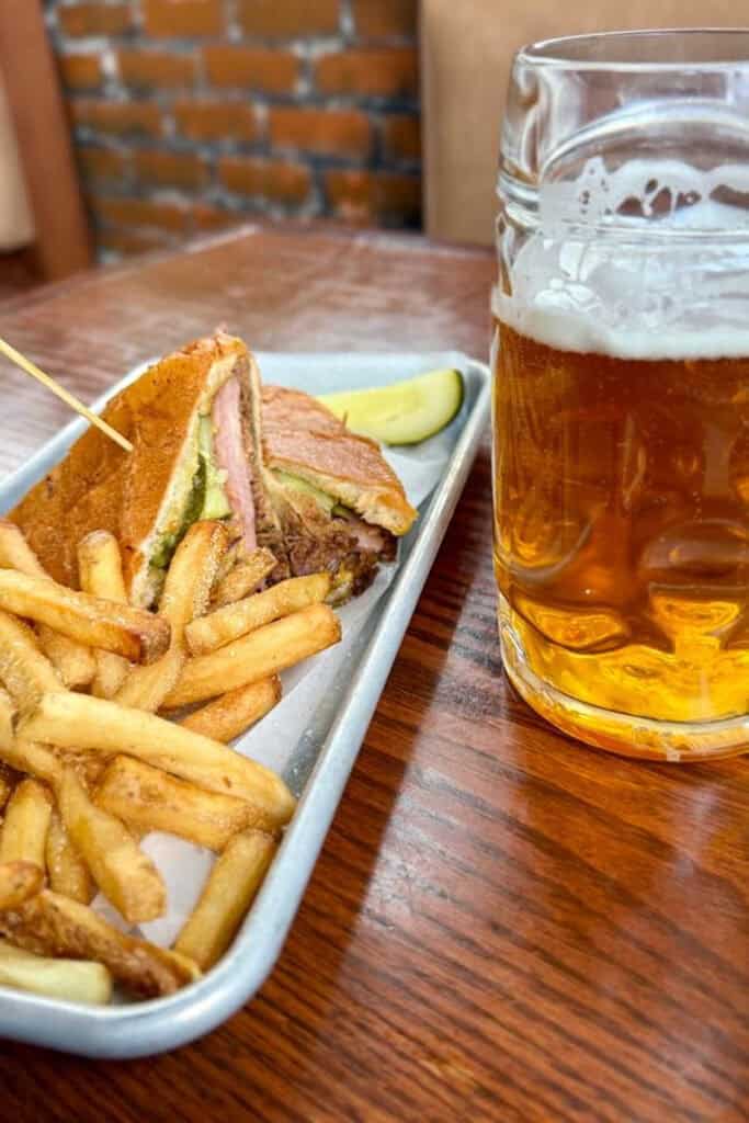 Sandwich and fries on tray next to glass of beer.