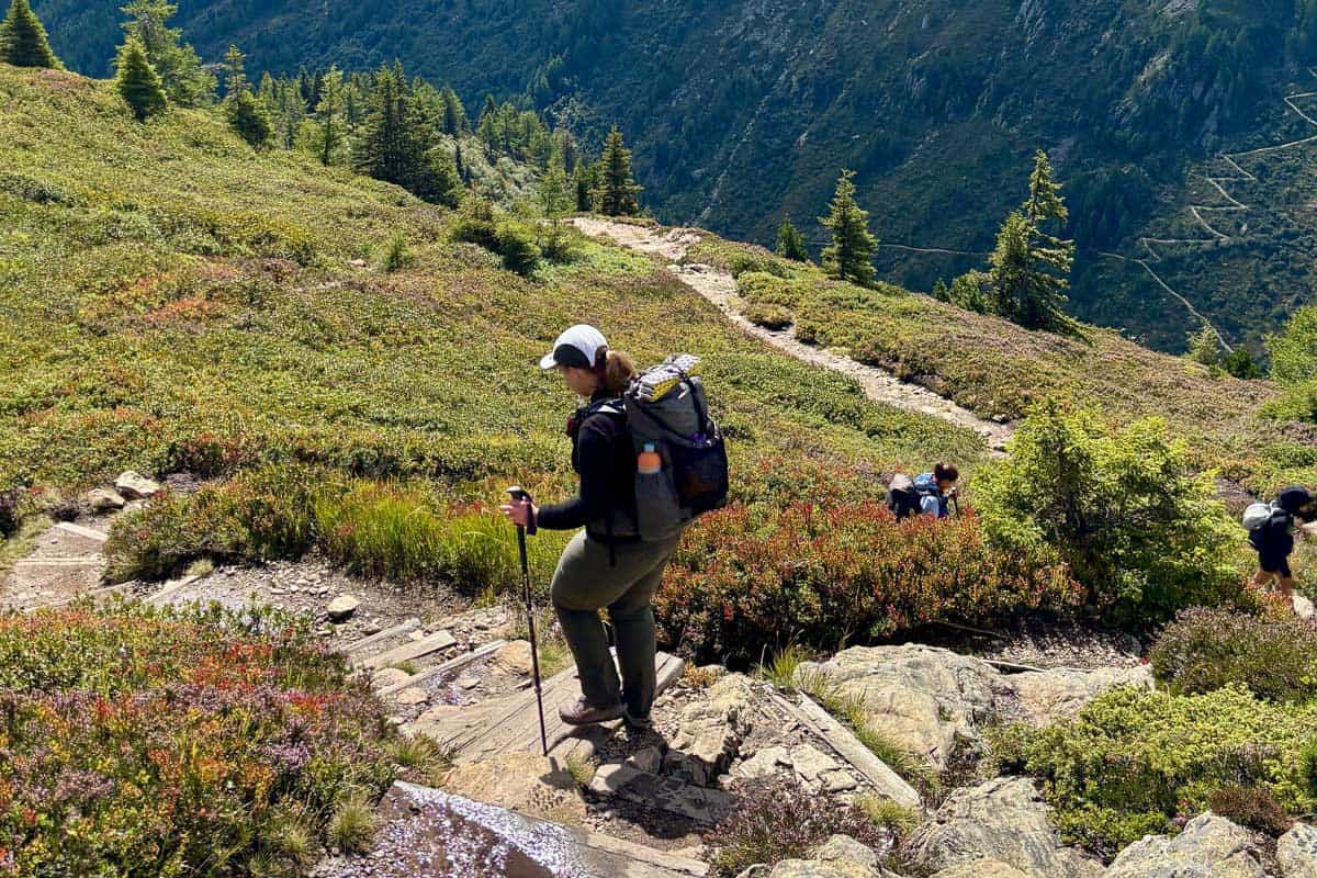 Hiker with backpack and trekking pole descending rocky hillside.