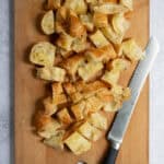 Chopped up pieces of croissant on cutting board with knife.