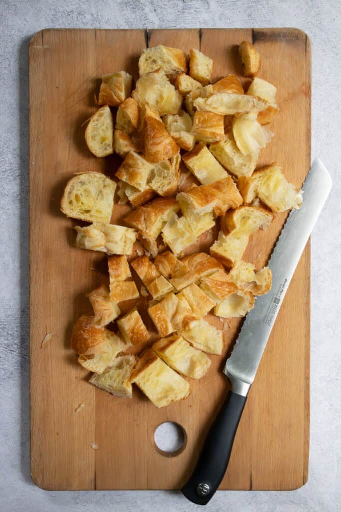Chopped up pieces of croissant on cutting board with knife.