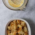 Casserole dish full of pieces of croissant next to mixing bowl full of custard.