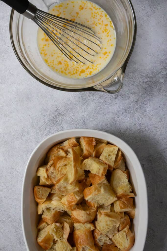 Casserole dish full of pieces of croissant next to mixing bowl full of custard.