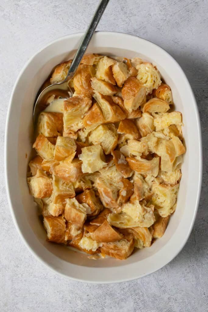 Pieces of croissant French toast soaked in custard in casserole dish.