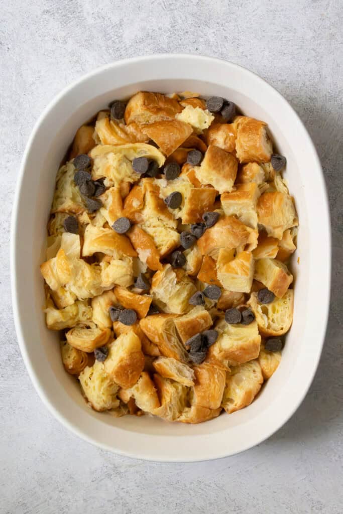 Pieces of croissant in casserole dish with chocolate chips sprinkled in.