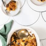 Baked croissant French toast with chocolate chips in a casserole dish next to plates with individual servings.