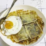 potato rosti with melted raclette and an egg on a plate.