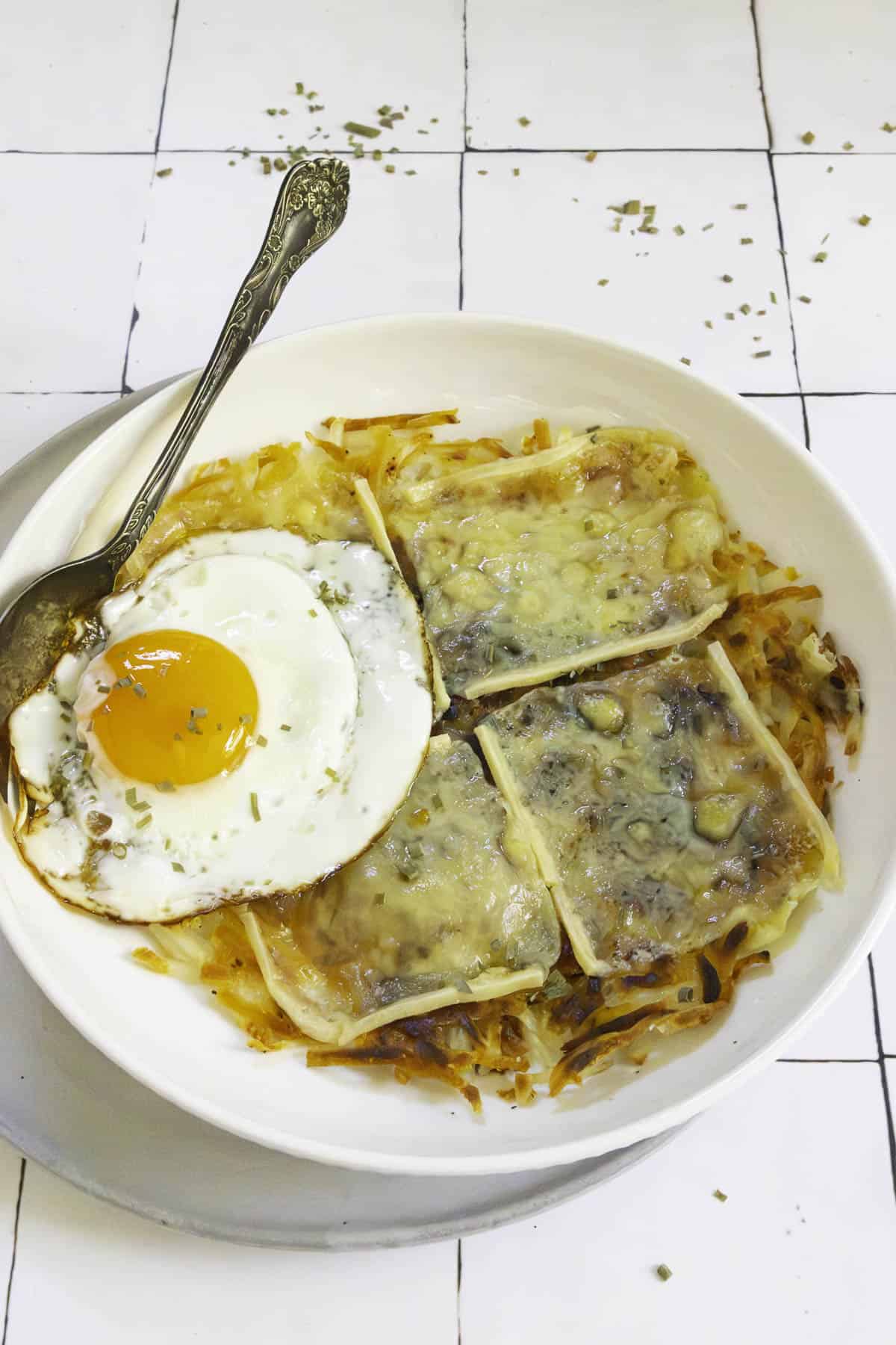 potato rosti with melted raclette and an egg on a plate.