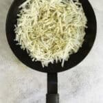 shredded potatoes and seasoning in a pan.