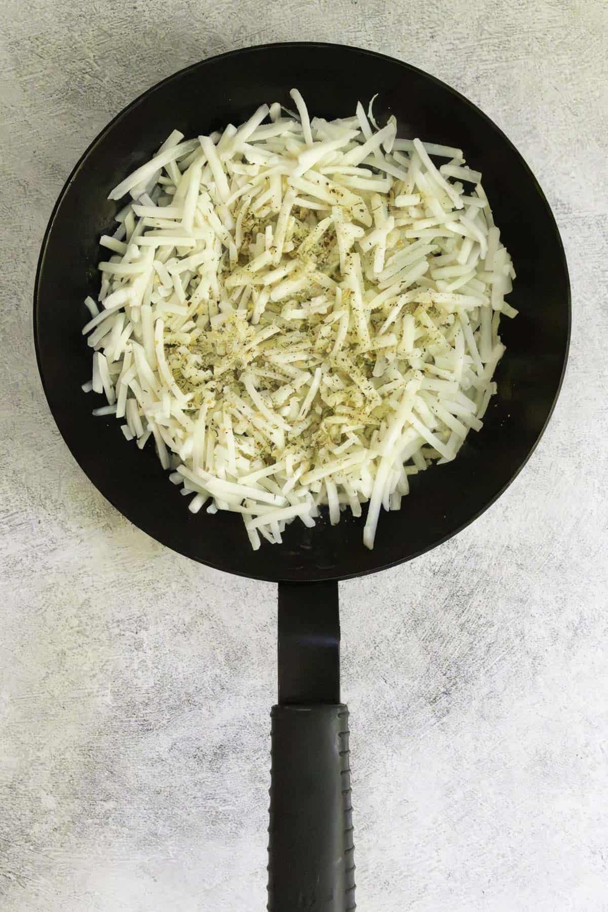 shredded potatoes and seasoning in a pan.