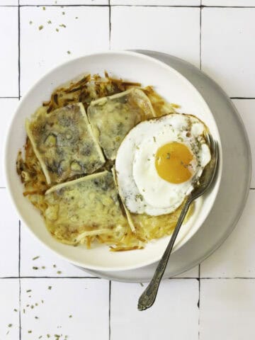 potato rosti with melted raclette and an egg on a plate.