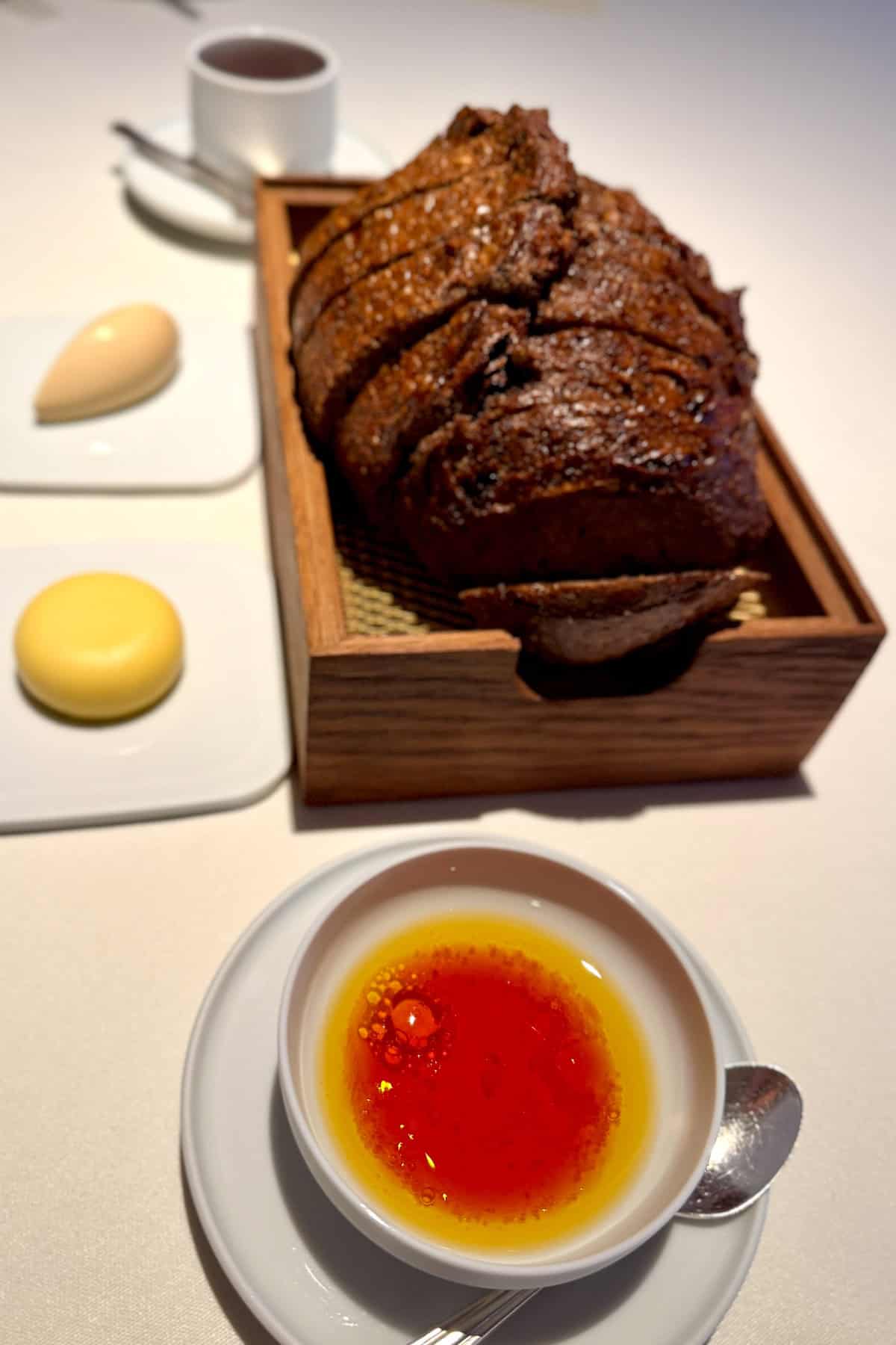 Small loaf of malted barley sourdough with pats of butter and a dish of sauce.