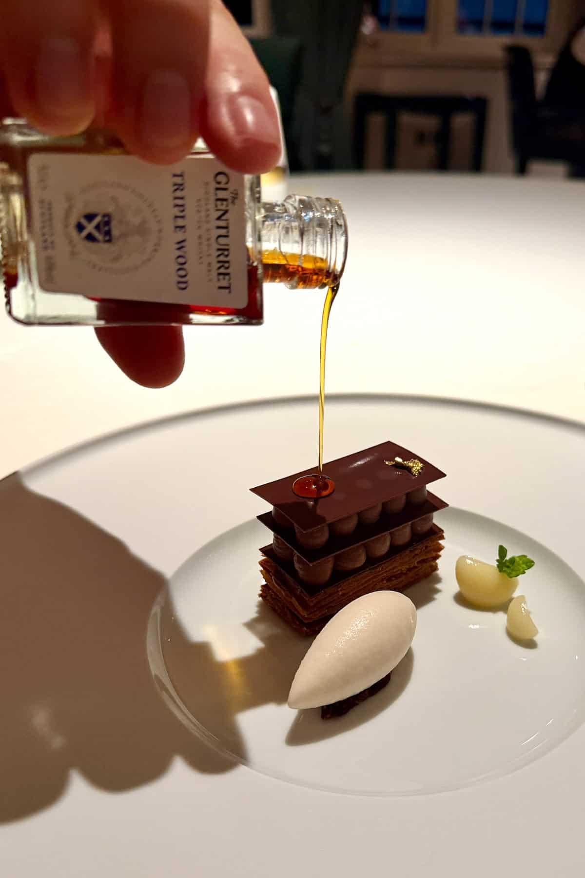 Pouring whisky from a small bottle over mille-feuille pastry.